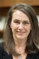 Smiling woman headshot, shoulder-length brown hair, black blazer, blurred bookshelf background